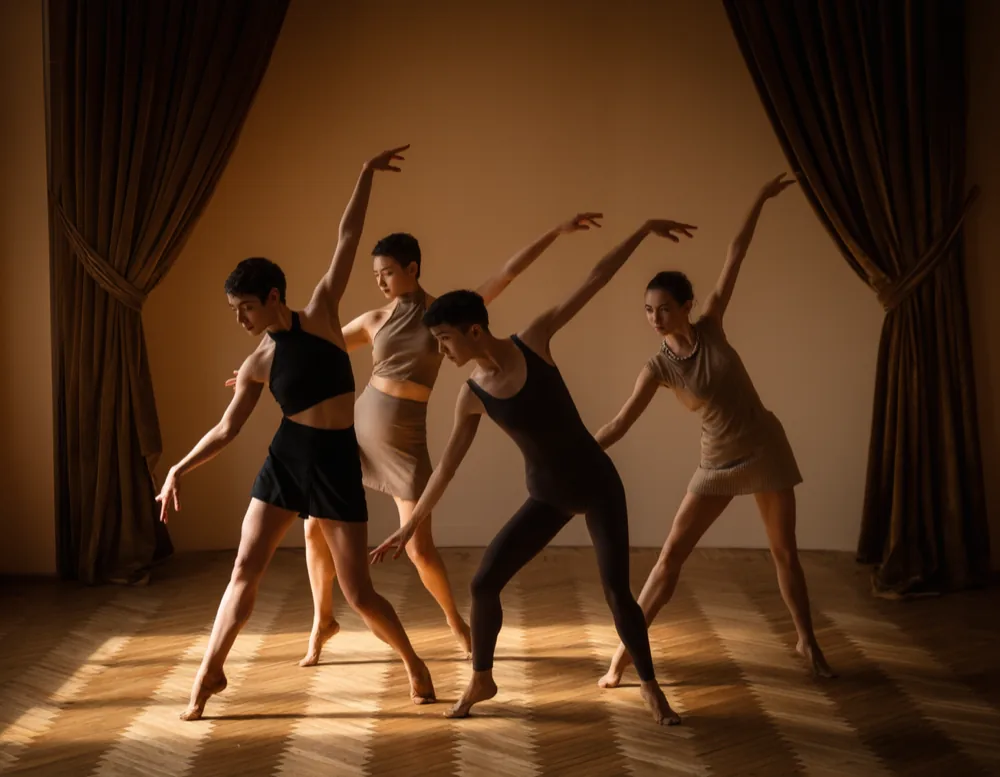 Four dancers holding a sharp jazz position on parquet with the velvet drapes open behind them